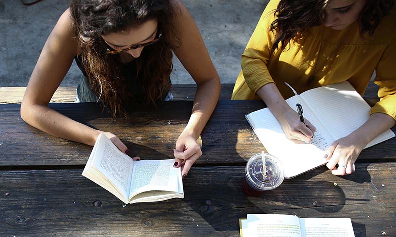 Two women sitting at a table with open books.